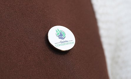 A white, round .75 inch pin with the Quinte Conservation logo.